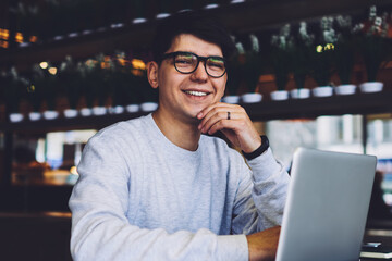 Portrait of happy successful graphic designer looking at camera during working process with laptop device.Smiling freelancer sitting at modern computer and using free high speed internet connection