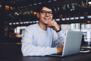 Portrait of happy successful graphic designer looking at camera during working process with laptop device.Smiling freelancer sitting at modern computer and using free high speed internet connection