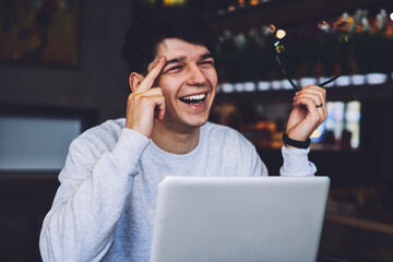 Emotional student understood mistake during working on new website at laptop computer in coworking space.Happy successful young man with optical eyeglasses in hand sitting at computer