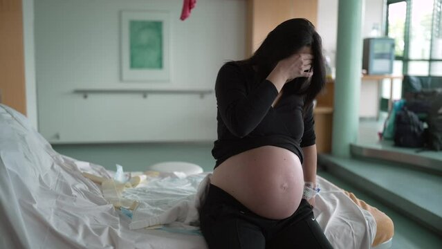 Pregnant woman suffering from contractions during pre labor at clinic covering face in pain, expecting mother at hospital waiting for childbirth