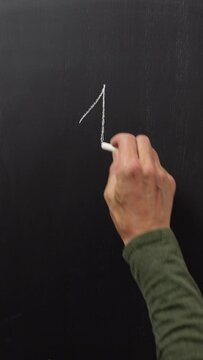 Close-up shot of a hand writing 1+1=2 on a blackboard, symbolizing the basic sum of one plus one equals 2. Vertical video