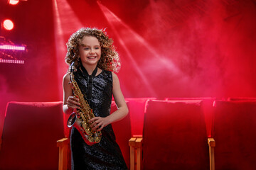 A young musician girl holds a saxophone and smiles.