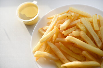 French fries on a white plate with sauce. Delicious fried crispy potatoes.