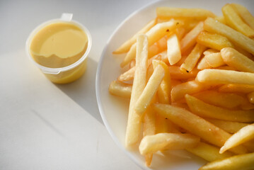 French fries on a white plate with sauce. Delicious fried crispy potatoes.