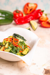 Fresh cucumbers, bell peppers, and herbs on white plate, pink background