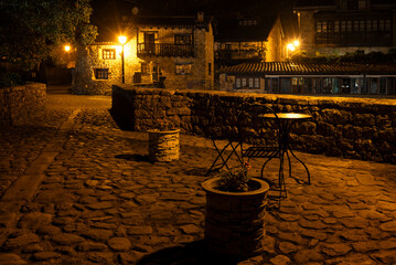 A stone walkway over the old bridge with a few tables and potted plants. The scene is quiet and peaceful at night. Barcena Mayor, Saja-Besaya Natural Park, Cantabria, Spain