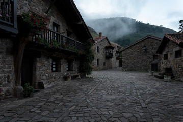 A quiet, empty courtyard with a few houses in the background. Fog falling over the houses in a dark and calm atmosphere. Barcena Mayor, Saja-Besaya Natural Park, Cantabria, Spain.