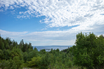 panoramic view of the forest with hills and the sea against a background of blue sky with clouds