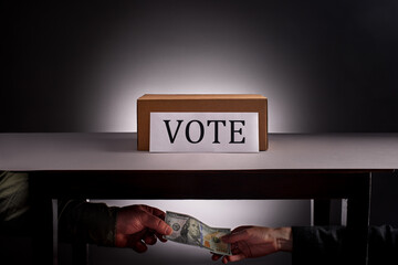 Hands holding hundred dollar bill under table with voting box