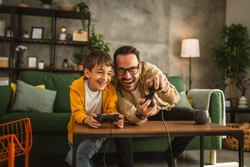 Father and son play video games with joystick and have fun at home