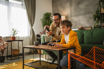 Father and son play video games with joystick and have fun at home