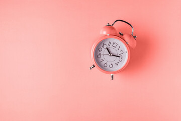 Coral color alarm clock on bright background. Minimal concept.