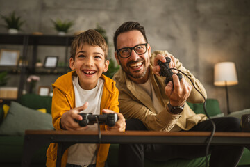 Father and son play video games with joystick and have fun at home © Miljan Živković