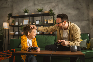 Father and son play video games with joystick and have fun at home