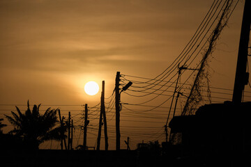 Low setting full round sun with electricity and telephone cable wires in silhouette, Accra, Ghana