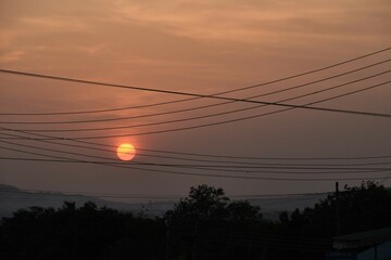 Close up view of low setting full round sun with electricity and telephone cable wires in...