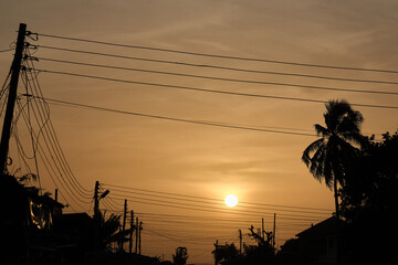 Low setting full round sun framed with electricity and telephone cable wires and palm trees in...
