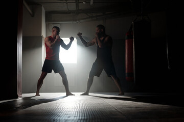 Two backlit male figures with clenched fists standing in front of one another and practicing basic...