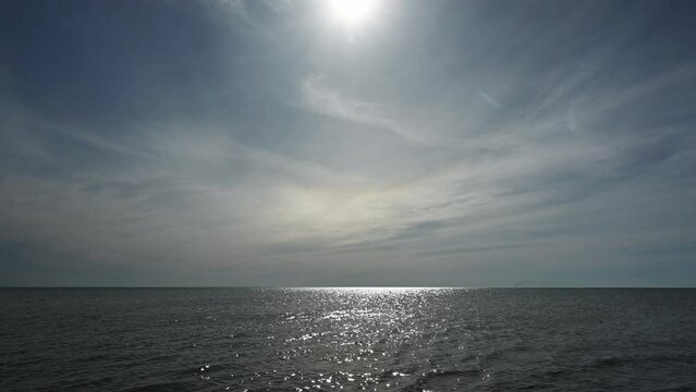 Water sparkling in a large lake under a blue sky filled with wispy clouds. The sun creates sun-rays at the top of the clip.
