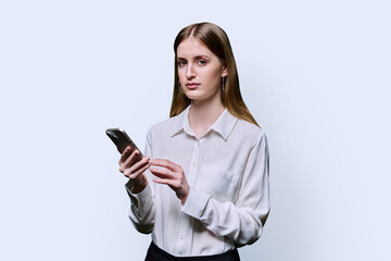 Teenage student girl in shirt holding smartphone in hands on white studio background
