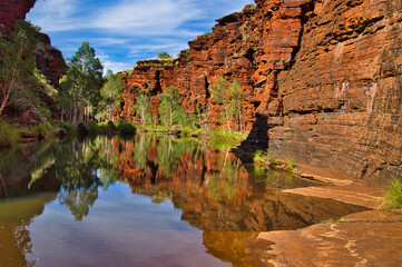 Red rocks and green trees reflecting in the clear water of a pool in the Kalamina Gorge, Karijini National Park, Western Australia
