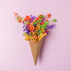 Ice cream cone with a colorful party streamers on pink background. Minimal party concept. Flat lay.