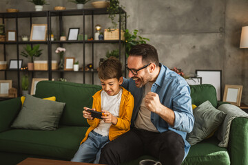 Father and son play video games on a mobile phone and enjoy at home