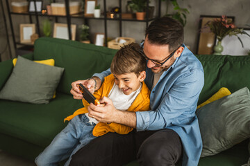 Father and son play video games on a mobile phone and enjoy at home