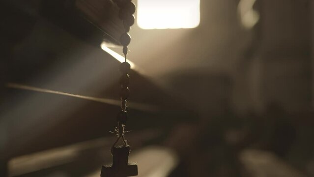 Wooden prayer beads hanging from Bible and swinging close up handheld shot. Christian rosary with cross and psalmbook religious symbols in church