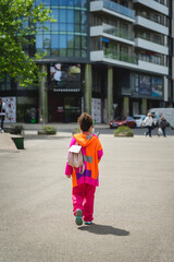 Girl in vivid cloth walking at street, rear view. Modern city life. Regular people out in public places