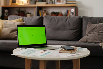Round table with laptop, unpaid bills and financial documents, mobile phone and notepad standing by couch in living room