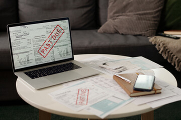 Laptop with online document with past due stamp standing on round table with other bills and...