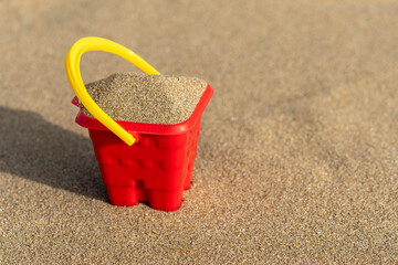 Red sand castle bucket on a sand background. Minimal summer vacation concept.