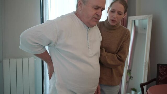 Elderly man feels sudden lower back pain, slowly walks to bed with his daughter support to sit down.