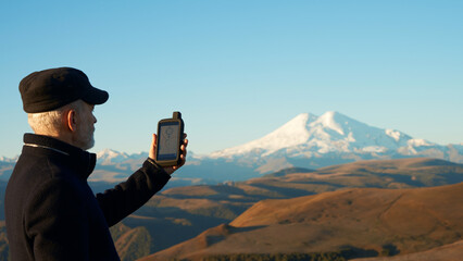 Adult man with GPS navigator in his hand on the background of mountain relief with Elbrus in the...