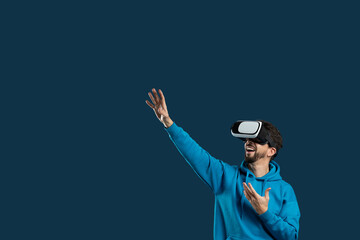A man wearing a blue hoodie is immersed in a virtual reality experience while wearing a headset. He...