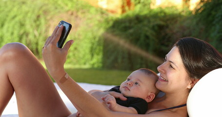 Mother taking selfie with baby son outside by the poolside