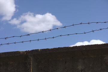 A concrete wall with barbed wire on top against a blue sky background
