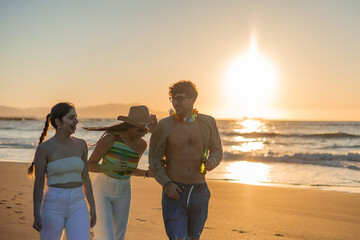 Three Multicultural Friends Laugh as They Stroll Relaxingly on the Beach at Sunset with Beers