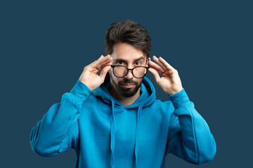 A focused man with a beard and tousled hair is adjusting his glasses and looking straight ahead. He...