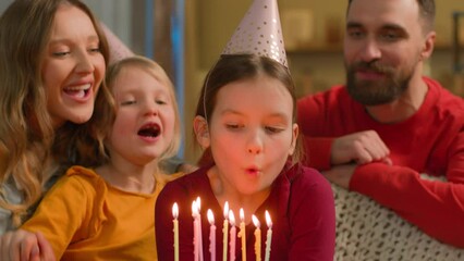 Caucasian family sing happy birthday little girl child daughter blow cake candles wish celebration funny joyful parents kids children siblings sisters in festive hats celebrate birth event party home