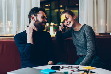 Smiling trendy friends with sticky notes on their foreheads playing joyful name game while gathered together at cozy cafeteria, cheerful successful male and female resting and having fun indoors