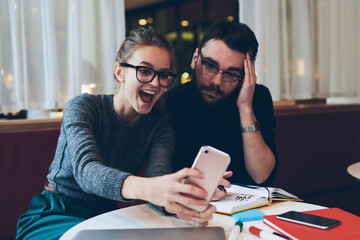 Young emotional female persons with best friend using smartphone application for video call sitting...