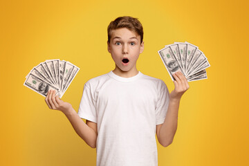 Finance, investment and money saving. Excited boy man holding lots of dollars, orange studio...
