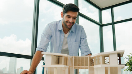 Portrait of engineer in casual outfit smiling at camera while inspect house model. Skilled...