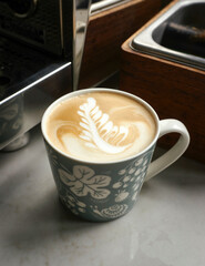 Intricate and beautiful foam latte art on a cappucino style coffee drink. A bespoke Italian professional espresso machine in the background.