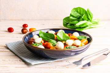 Fresh homemade caprese salad with baby mozzarella cheese, cherry tomatoes, basil leaves and olive oil on rustic wooden table close up. Country style dinner concept.