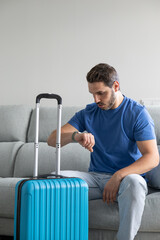 Man checking the time before catching a flight with suitcases prepared at home