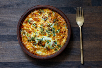 Ceramic bowl with vegetable frittata, simple food. Frittata with eggs, pepper, onion, greens and cheese on wooden table, closeup, top view. Italian egg omelette