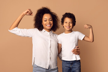A smiling African American woman and a young boy are flexing their muscles together, showcasing a...